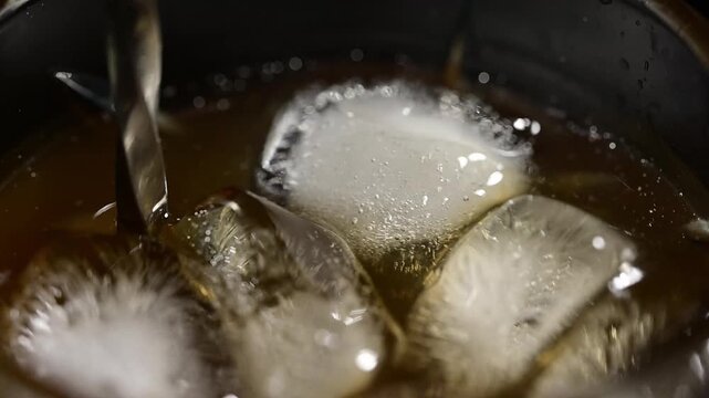 Top view of glass with alcoholic cocktail and ice cubes, bartender spoon stirring drink slowly on black background, mixing motion, cold refreshing beverage, professional bartending process