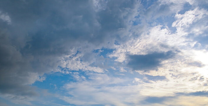 Majestic dramatic sky landscape with heavy dark rain clouds mixing with bright white clouds and light blue patches, capturing dynamic nature weather changes, wide-angle shot.
