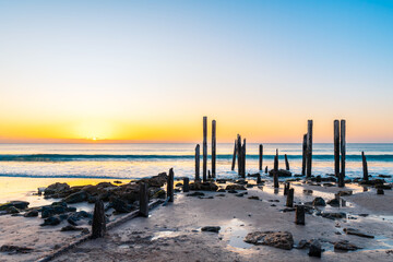 Fototapeta premium Historic petrified timber posts and stone foundation remains of the former Port Willunga jetty at sunset on the Fleurieu Peninsula, South Australia. 