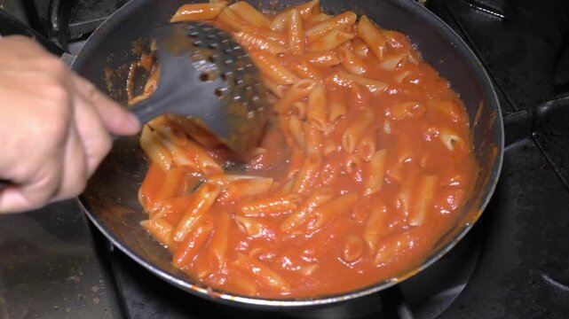 Freshly cooked pasta is tossed in sauce to blend flavors before serving guests during a restaurant meal service.