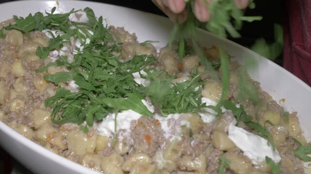 Fresh arugula leaves are scattered over plated gnocchi topped with white ragu sauce and creamy burrata, adding a peppery finishing touch to this elegant dish for the party guests