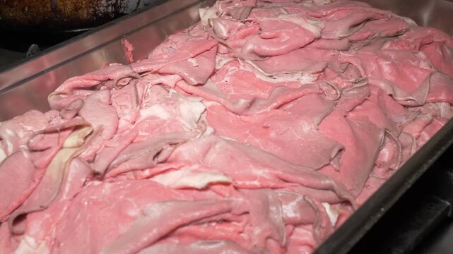 Thin strips of raw beef straccetti are neatly arranged in a tray in the restaurant kitchen, prepared and ready to be cooked for a flavorful dish at the catered party.