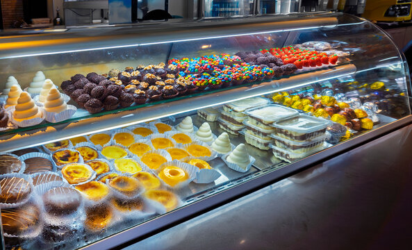 A glass display case in a confectionery shop filled with various Brazilian sweets like brigadeiros, quindins, pastel de nata, honey cakes (p&atilde;o de mel), and assorted chocolates.
