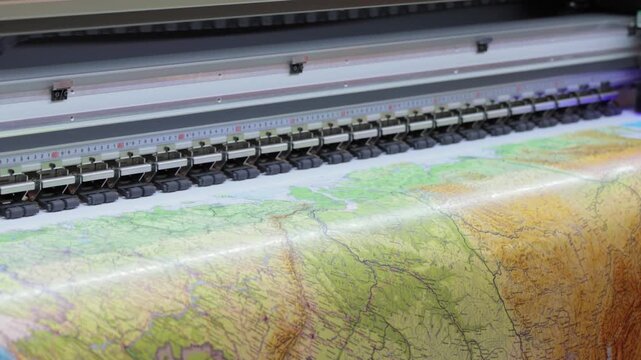 Large format printer head moving across a detailed map printing on vinyl material close up shot.