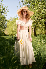 Fototapeta premium Young woman in elegant summer outfit enjoying a sunny day in a blooming orchard