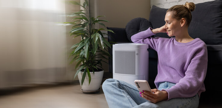 smiling woman sitting on the floor by air purifier in living room. air quality and microclimate control at home