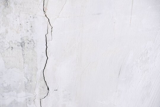Vertical fracture on white weathered plaster wall surface