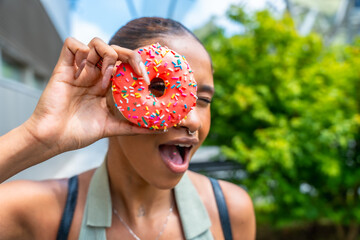 Obraz premium Young woman playfully holding pink donut over eye