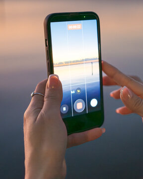 Person Recording Sunset Video on Smartphone by the Water