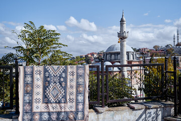 Obraz premium Traditional patterned rug hanging on a railing with Istanbul mosque, minaret, trees and blue sky in the background.