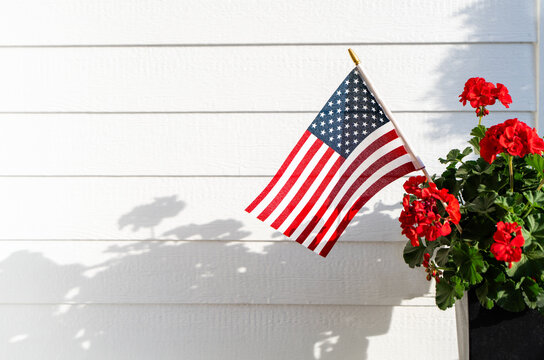 Small American Flag with Red Geraniums Against White House Siding