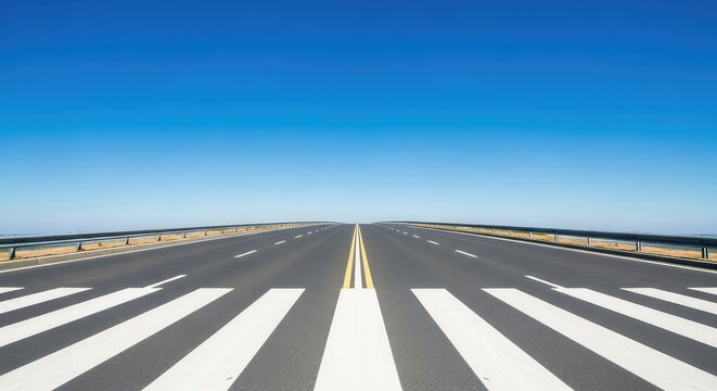 A symmetrical frontal perspective of an asphalt urban road featuring a clean white striped zebra crossing under a bright clear blue sky, crosswalk, symmetry, minimal
