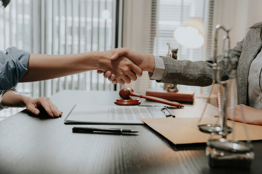 A close-up image of a lawyer and client shaking hands after reaching a legal agreement, and also shaking hands with a business partner regarding a contract in court and with the gavel.