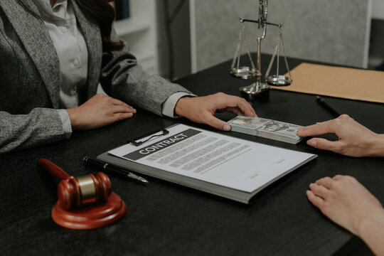 Close-up of person giving bribe money in US dollars to a judge or lawyer at desk.