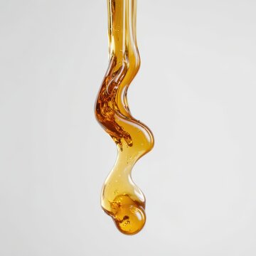 Single amber liquid drop falling with thick golden honey texture and air bubbles visible inside suspended viscous fluid creating elegant drip motion on clean cream colored background.