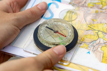 Orienteering compass on a topographic map, hands holding navigation equipment, concept of hiking, adventure, travel, and wilderness survival. © Lana Pietukhova
