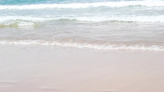 Ocean waves rolling onto a sandy beach with a curving coastline and distant headland along the Spanish coast under a clear sky.