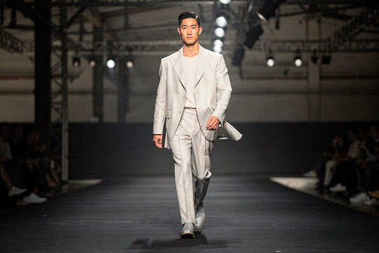 Male Asian model walking on a fashion runway wearing a stylish light grey linen suit at a catwalk show