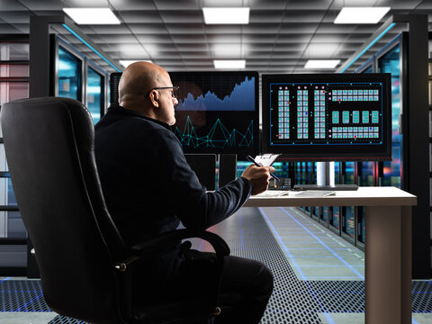 Data center management. IT operator monitors server room infrastructure and network analytics on screens for digital system control.