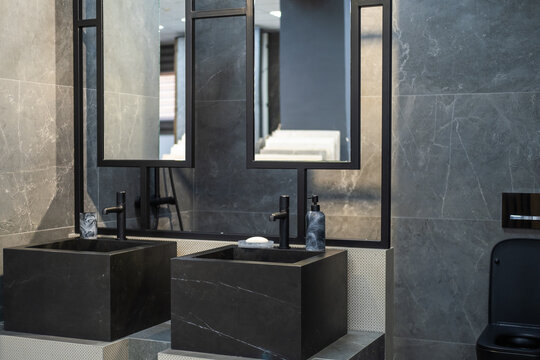Contemporary bathroom interior featuring a black toilet, stone vessel sink and dark marble-effect wall tiles. Modern residential design, elegant fixtures, minimalist style, premium finishing materials