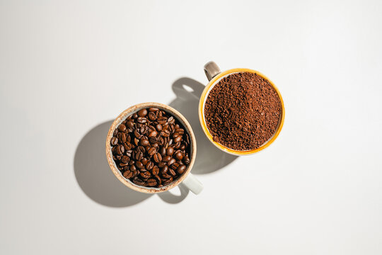 Roasted coffee beans and ground coffee in cups on white background, flat lay with copy space