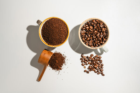 Roasted coffee beans and ground coffee in cups on white background, flat lay with copy space