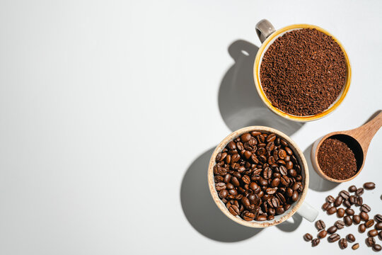 Roasted coffee beans and ground coffee in cups on white background, flat lay with copy space