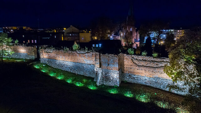 Aerial view of the illuminated medieval city walls and a church tower at night in Debrzno, Pomeranian Voivodeship, Poland.