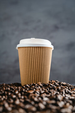Takeaway coffee cup surrounded by roasted coffee beans on dark background, template with design space