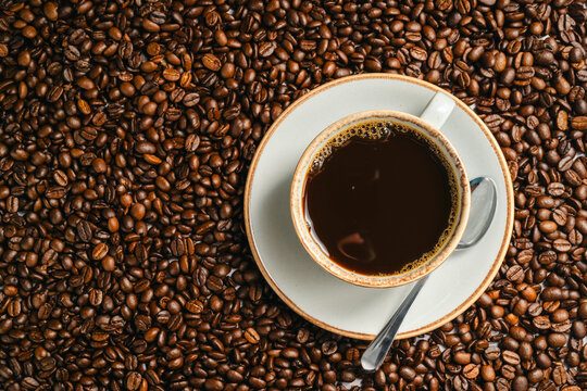 Cup of black coffee on roasted coffee beans background, top view