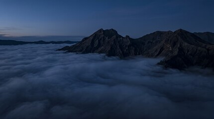 Fototapeta premium Aerial view of rugged mountains peeking through dense fog at dusk.