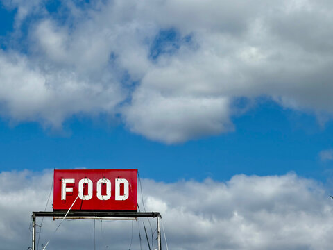 Vintage Roadside Food Sign Against Blue Sky and Clouds with Copy Space