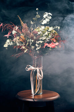 Autumn bouquet in glass vase with ribbon on stool in smoky studio