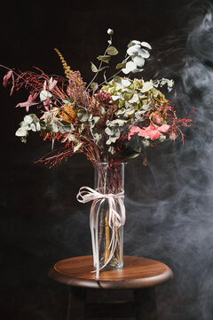 Autumn bouquet in glass vase with ribbon on stool in smoky studio
