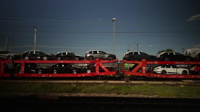 Industrial view from a train window near Ingolstadt in Bavaria, Germany, showing a long freight train loaded with brand new cars on a car carrier wagon from the local automotive factory.