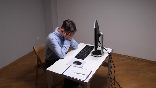 Stressed person sitting at a desk with hands covering face, experiencing frustration, failure, and workplace burnout while working at an office computer