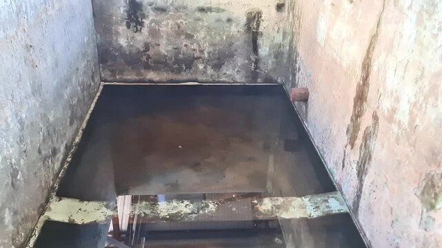 Abandoned weathered concrete water tank with stagnant dirty water and industrial roof reflection