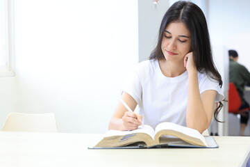 Naklejka premium Asian woman reading book in a library for education, studying and research in school, university or college campus. Focus, book and student at bookshelf for language learning or philosophy knowledge 
