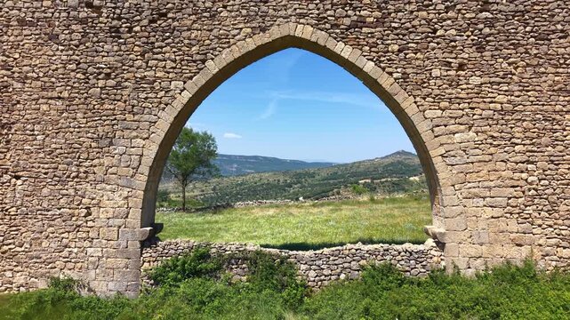 Aerial reverse flight video pulling back through a Gothic arch of the medieval aqueduct of Morella with parallax effect revealing the stone arcade structure and valley landscape, Castellon, Spain