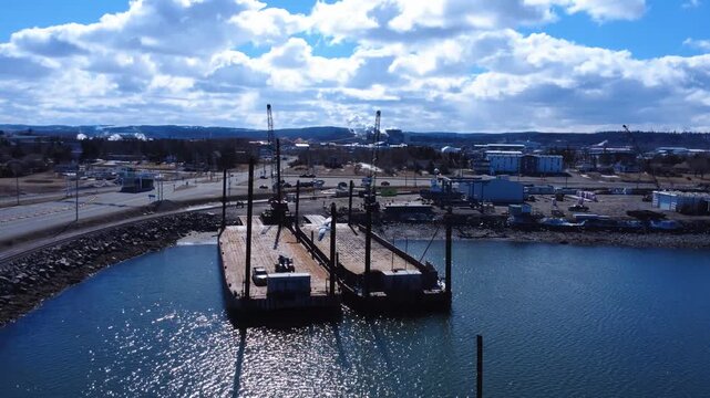 High-angle aerial shot of a working harbor in Matane, Quebec, with barges, cranes, roads, and industrial development.