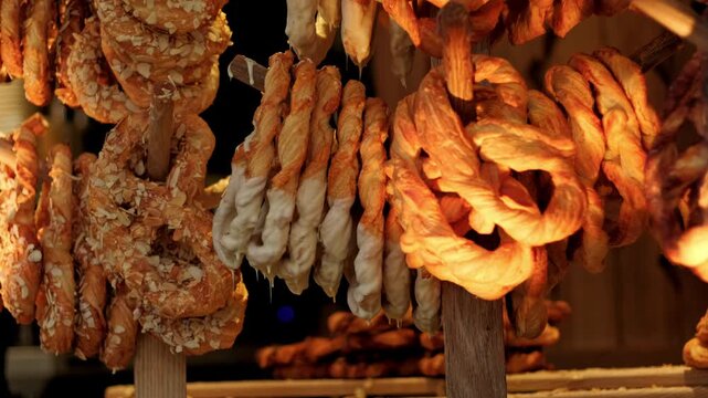 Golden pretzel hanging on wooden rack at market stall. Fresh baked pastry with almond and white glaze. Sweet snack product for Christmas fair shopping experience.