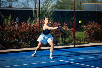 Obraz premium Woman playing padel on blue court hitting ball