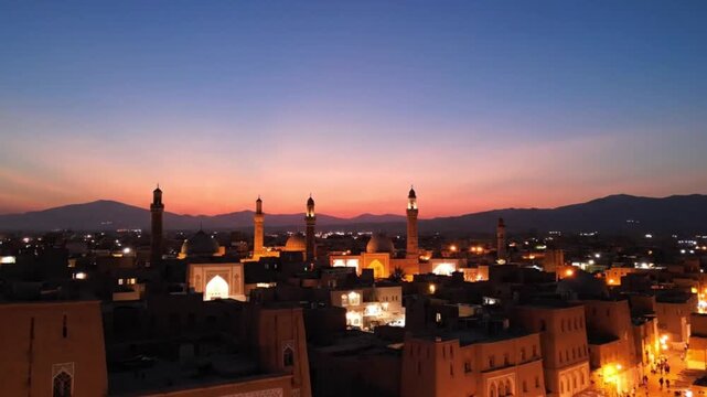 Aerial view of the historic city of yazd in iran at sunset, featuring traditional mudbrick architecture, minarets, and domes against a mountain backdrop