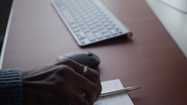 Close up on hands of African American man writing in notebook then typing on wireless keyboard at office desk. For corporate training videos, remote work advertisements, or software development promos