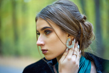 A woman in an elegant turquoise dress poses gracefully in the street. She stands against the background of green grass. © SergeiPh