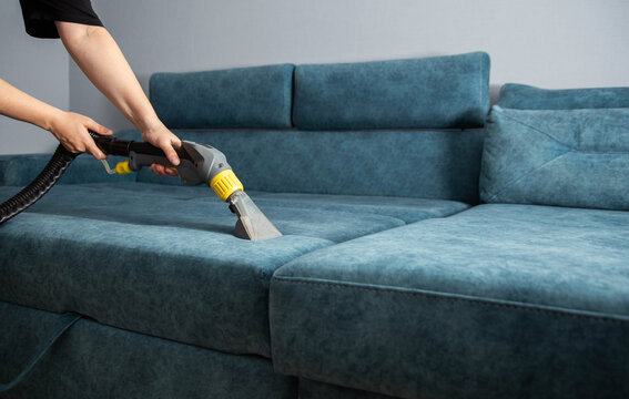 Person cleaning blue fabric sofa with wet vacuum cleaner for deep upholstery maintenance. Professional hygiene service for home furniture.