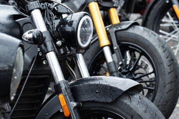 Fototapeta premium Close-up detail of front section of black motorcycle, featuring modern LED headlight, front fender, and chrome shock absorbers, surface covered with water drops after rain