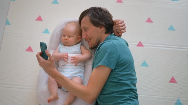 Happy father showing baby on phone at home.