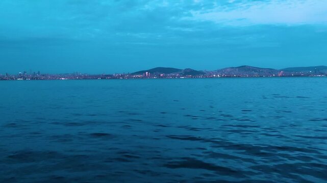Panoramic view of the Sea of Marmara and distant Istanbul city coastline with glowing night lights during twilight blue hour, filmed from Kinaliada.