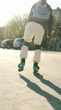 Girl wearing inline skates and a backpack glides on a large paved lot. Sun creates bright backlight and long shadows.